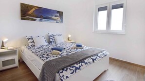 Ein Schlafzimmer mit einem Bett, zwei Nachttischen, einem Fenster und einem Bild an der Wand.