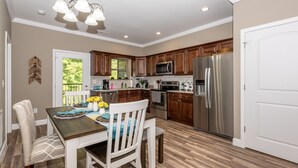 A modern kitchen with wooden cabinets, stainless steel appliances, and a dining area with a wooden table and chairs. - It is Springtime in TN- comfortable, clean, in a gated community & near food! (Townsend)