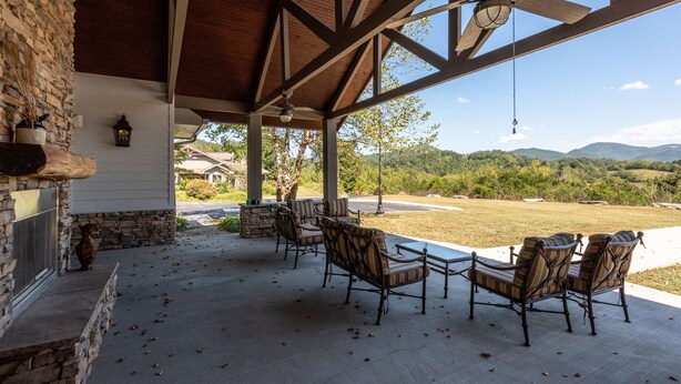 A covered patio with outdoor furniture, a stone fireplace, and a view of a green landscape. - It is Springtime in TN- comfortable, clean, in a gated community & near food! (Townsend)