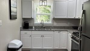 A modern kitchen with white cabinets, a stainless steel refrigerator, a gas stove, and a window providing natural light. - Cozy quiet Cottage (Deer Isle)