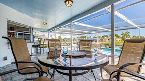 Eine Terrasse im Freien mit einem runden Tisch, Stühlen und Blick auf Pool und Palmen.