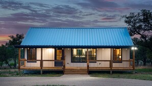 A two-story house with a blue metal roof and wooden porch. - The Armadillo Cabin | Great Back Porch (Fredericksburg)