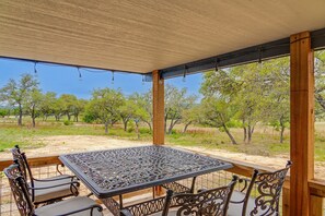 Un espace extérieur abrité, avec une table et des chaises en métal, entouré d’arbres et offrant une vue dégagée sur le paysage.