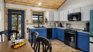A modern kitchen with blue cabinets, a black stove, and a microwave. - The Armadillo Cabin | Great Back Porch (Fredericksburg)