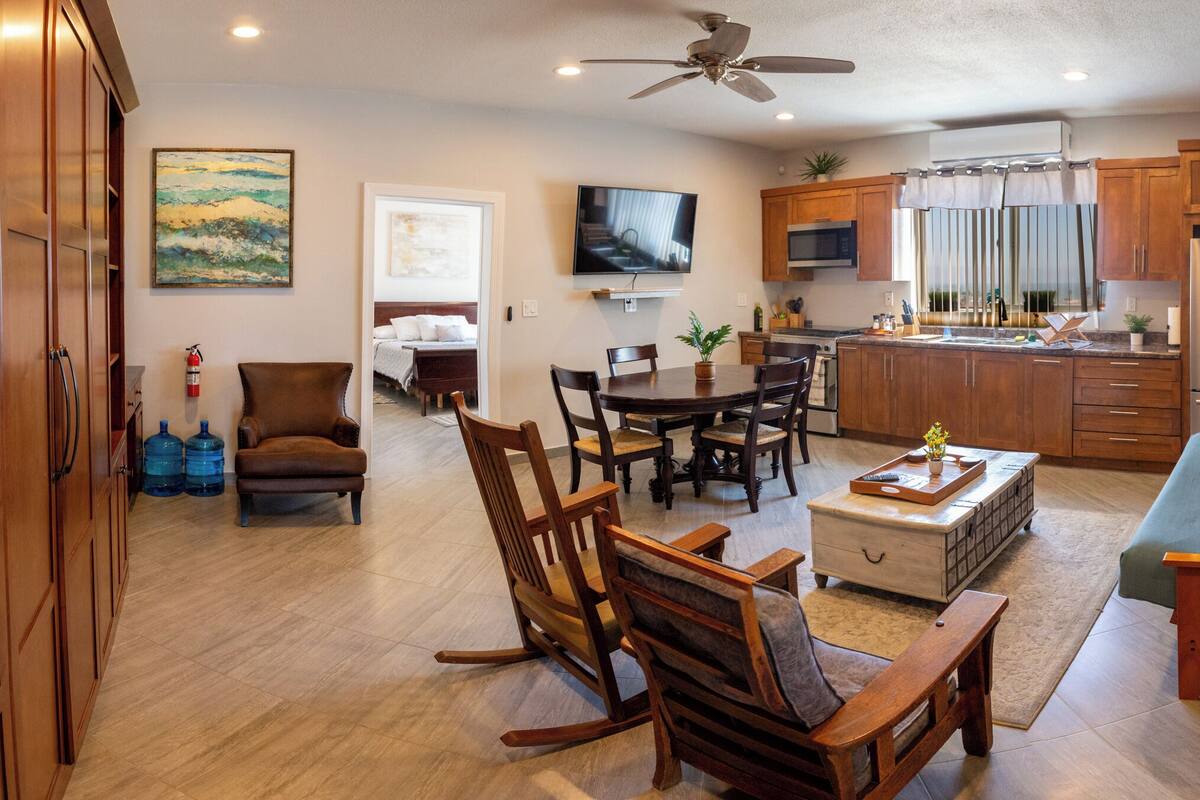 A spacious living area with a dining table, chairs, a sofa, and a TV mounted on the wall.
