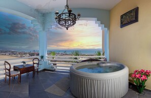 Una habitación con bañera de hidromasaje, una mesa de madera con sillas y vista a la playa.