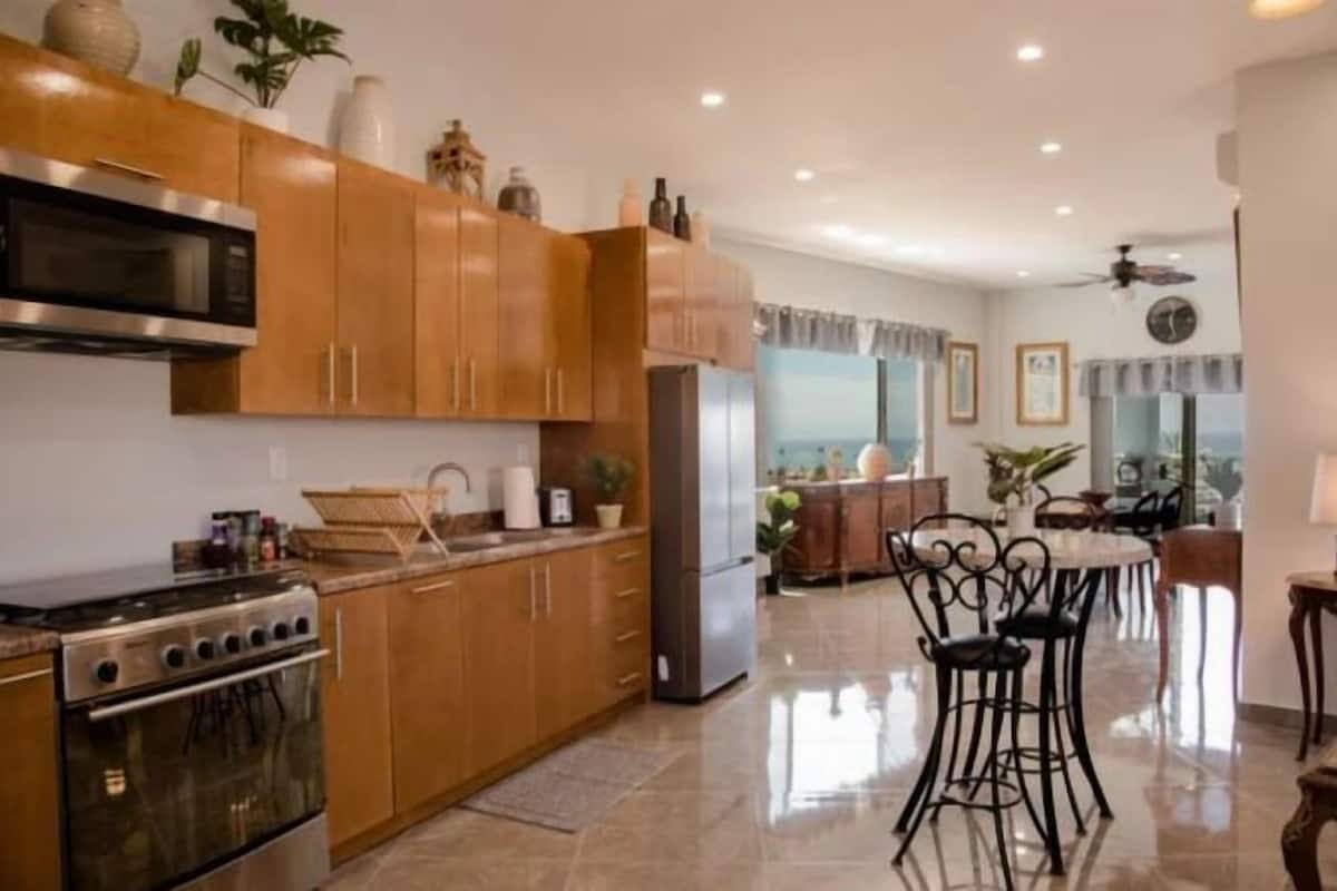 A modern kitchen with wooden cabinets, stainless steel appliances, and a dining area with black metal chairs.