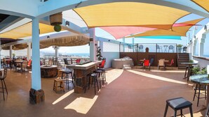 An outdoor bar area with stone walls, multiple seating options, and a view of the sea. - El Capitan Resort (Playas de Rosarito)