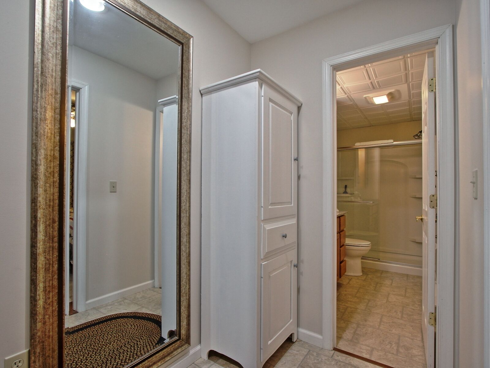 A hallway with a large mirror, a white door, and an open bathroom door leading to a shower area.