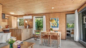 A modern kitchen with wooden cabinets, a dining area with a table and chairs, and a large window offering a view of greenery. - 3 bedroom lovely home in Sjællands Odde (Sjællands Odde)