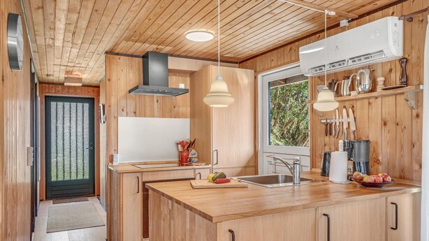 A modern kitchen with wooden cabinets, a central island, pendant lights, and a window with a view of greenery. - 3 bedroom lovely home in Sjællands Odde (Sjællands Odde)