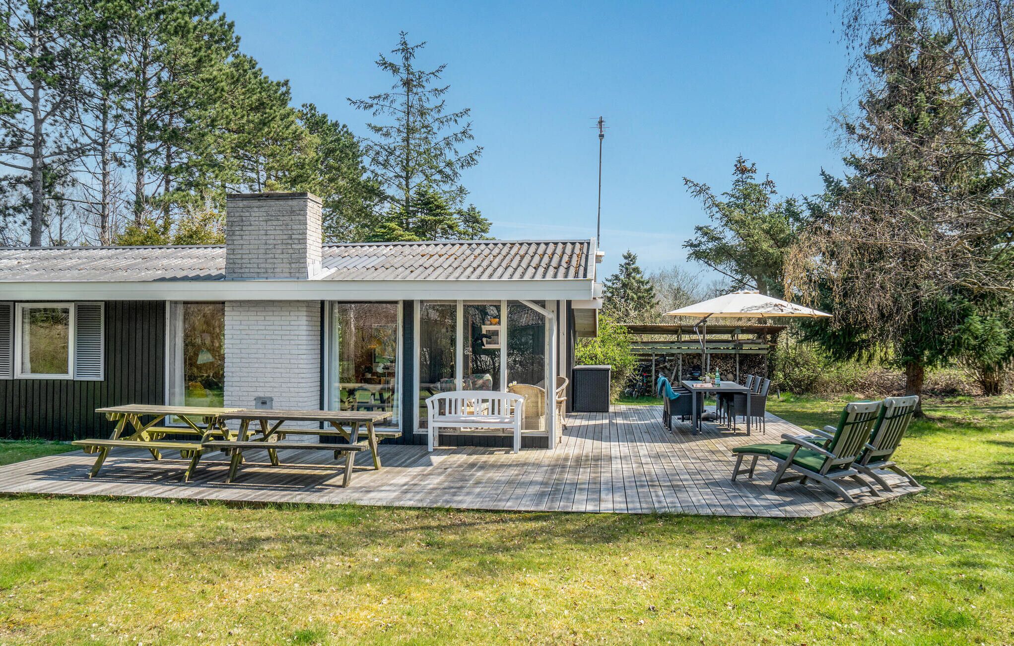 Ein modernes Haus mit einer Terrasse, einem überdachten Sitzbereich und einem großen Fenster mit Blick auf den Garten.