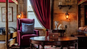 A cozy room with a red velvet chair, a wooden table, and a brick wall with framed pictures.