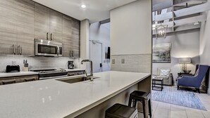 A modern kitchen with a large island, stainless steel appliances, and a seating area with a blue chair and a lamp. - Great Location Downtown, Heated Pool Access (Savannah)