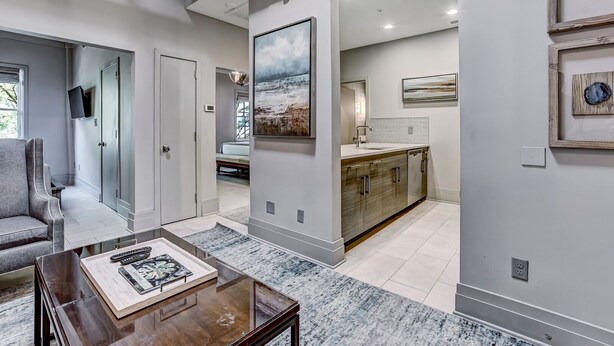 A modern living room with a large painting, a dining table with books, and a kitchen area with a large island and cabinets. - Great Location Downtown, Heated Pool Access (Savannah)