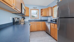 A modern kitchen with wooden cabinets, stainless steel appliances, and a window providing natural light. - 1747 - Resting Beach Place, Pool, Hot Tub & Game Room | Sleeps 15 in Corolla (Corolla)