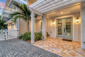 Welcome to a charming home with a covered porch, stone pillars, and a white picket fence, surrounded by lush greenery.