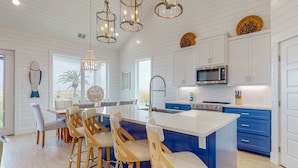 A modern kitchen with white and blue cabinetry, a large island with bar stools, and pendant lighting. - Golf Cart Included, Shared Pool, Hot Tub, Boardwalk to the Beach (Port Aransas)