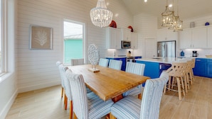 A spacious kitchen with white wooden walls, a wooden dining table, blue-striped chairs, and a blue island with bar stools. - Golf Cart Included, Shared Pool, Hot Tub, Boardwalk to the Beach (Port Aransas)