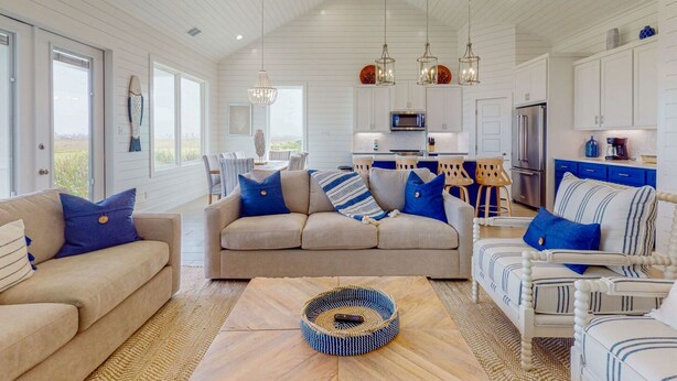 A spacious living area with a sofa and chairs, a coffee table, and a kitchen area with a refrigerator and microwave. - Golf Cart Included, Shared Pool, Hot Tub, Boardwalk to the Beach (Port Aransas)