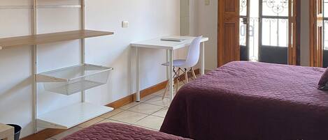 A room with two beds, a desk, a TV, and shelves.