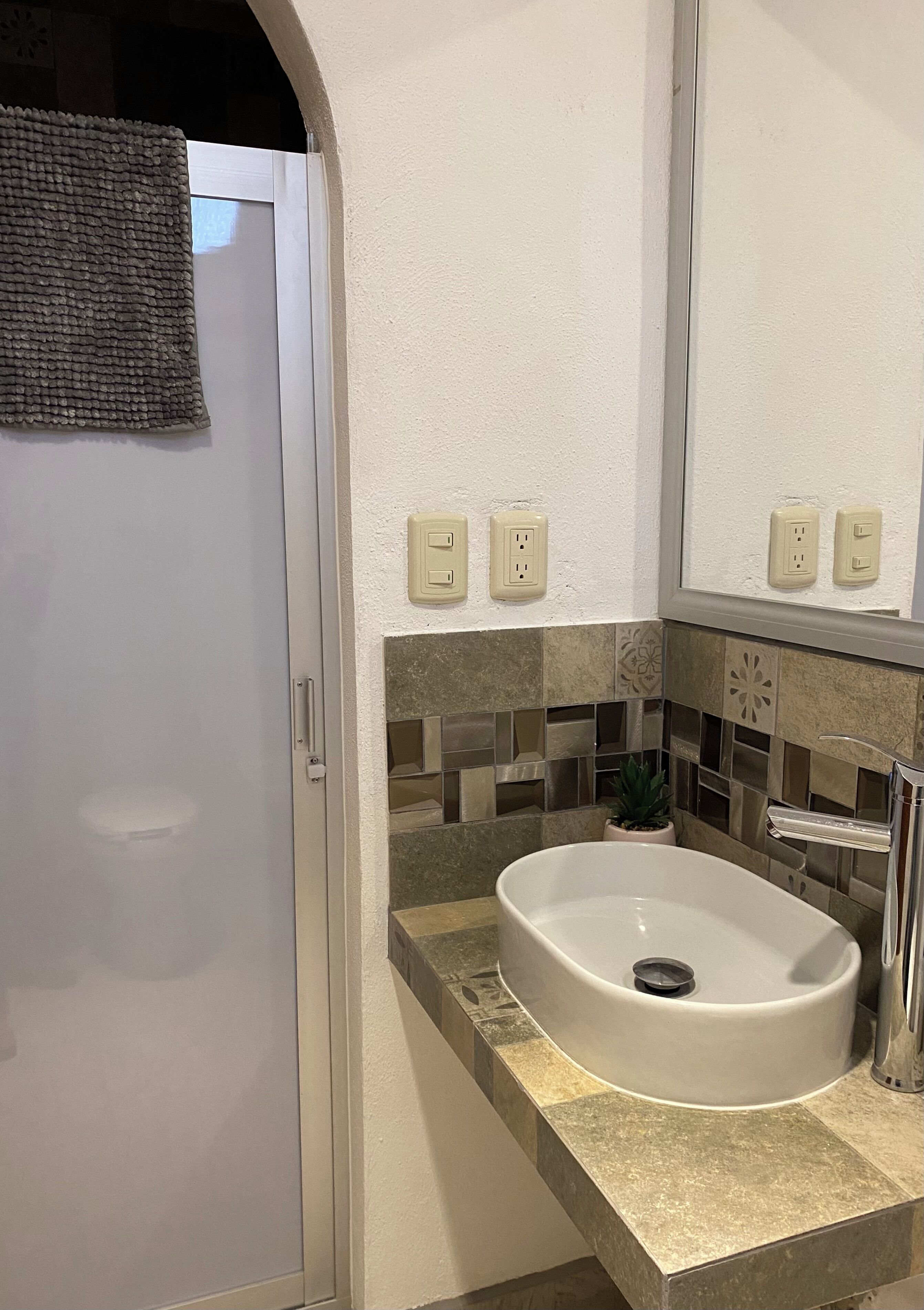 A bathroom with a white sink, a mirror, and a towel hanging on the door.