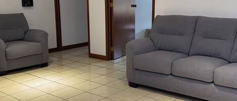 Una habitación con dos sofás grises, suelo de baldosas y una puerta con picaporte.