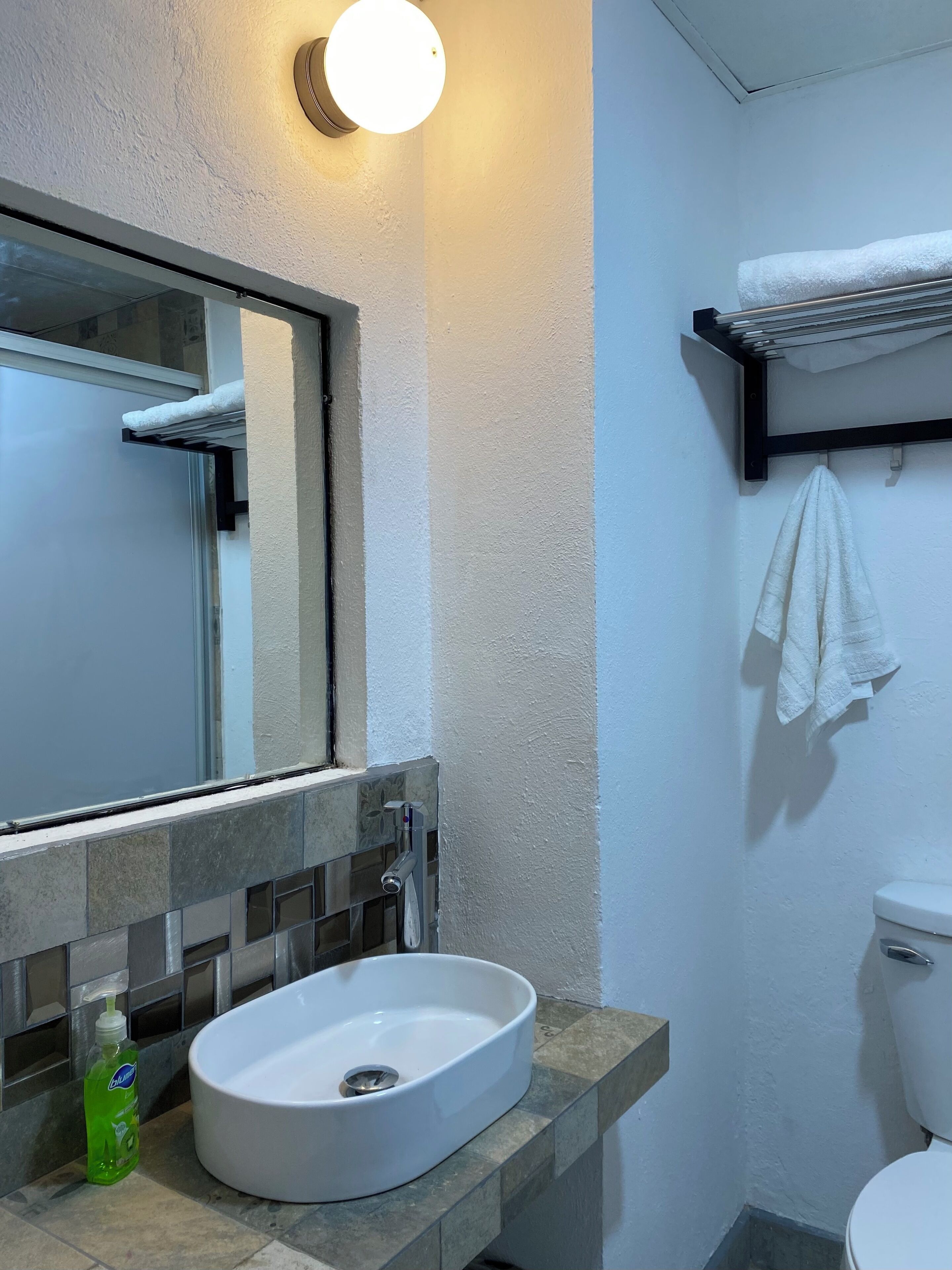 Un baño con un lavamanos blanco, un espejo, un toallero y un inodoro.