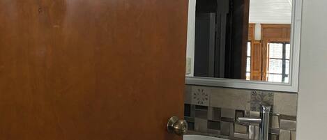 A bathroom with a white sink, a mirror above it, and a door with a brass handle.