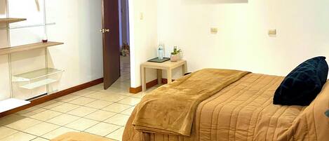 Habitación de hotel con dos camas, una mesita con una planta, un cuadro en la pared y una puerta que da a otra habitación.