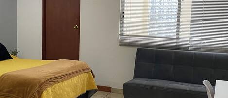 A room with a bed, a sofa, a door, and a window with blinds.