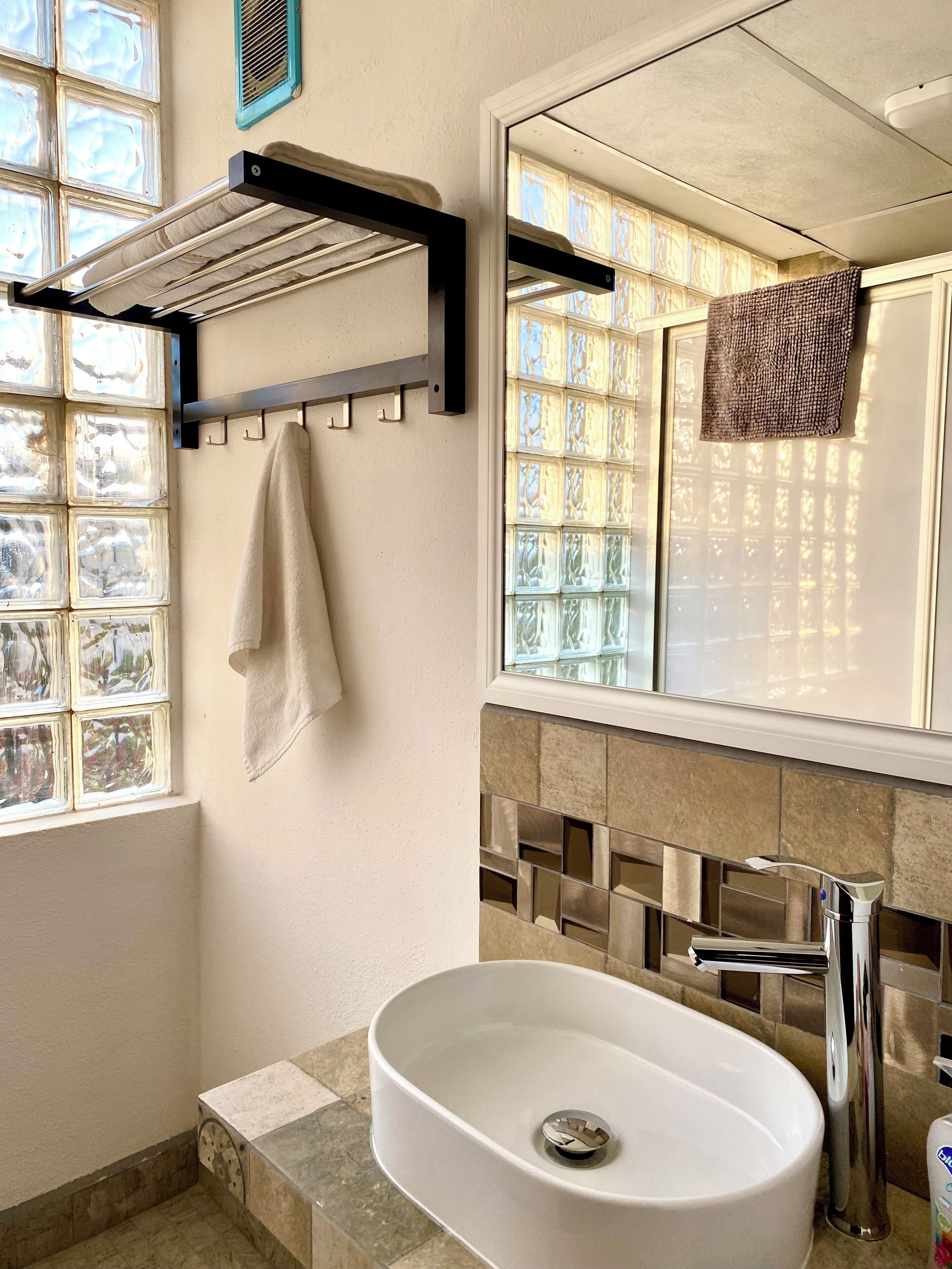 Un bagno con un lavandino bianco, un portasciugamani, una finestra con vetro decorativo e uno specchio.