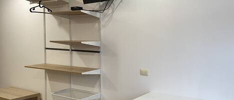 Una habitación con un escritorio blanco, una silla, una cama con una colcha roja y una estantería con un televisor.