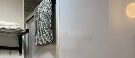 A bathroom with a glass shower enclosure, a towel rack with a white towel, and a toilet.