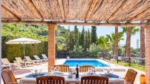 A covered outdoor dining area with a pool view, wooden chairs, and a table set for dining. - Cortijo La Reina by Solset (Torrox)