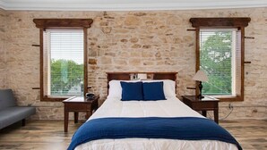 A bedroom with a stone wall, a bed with white and blue bedding, two nightstands, a lamp, and a window with blinds. - Historical Florence apartment (Florence)