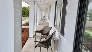 A covered outdoor corridor with white siding, two wicker chairs, and a concrete floor. - South Side Inn - Burlington (South Burlington)