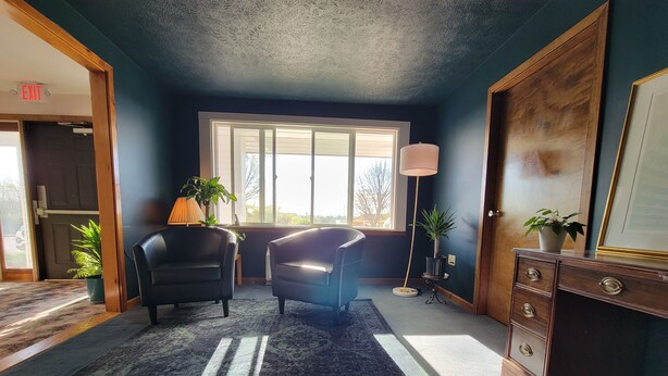 A room with a large window, two chairs, a desk, a dresser, and a lamp. - South Side Inn - Burlington (South Burlington)
