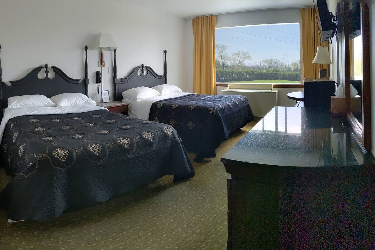 Una habitación de hotel con dos camas, un escritorio y una ventana con cortinas.