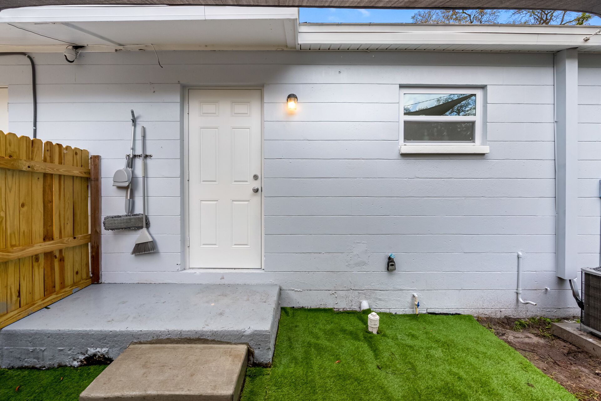 A house with a white door, a small window, a wooden fence, and a lawn.
