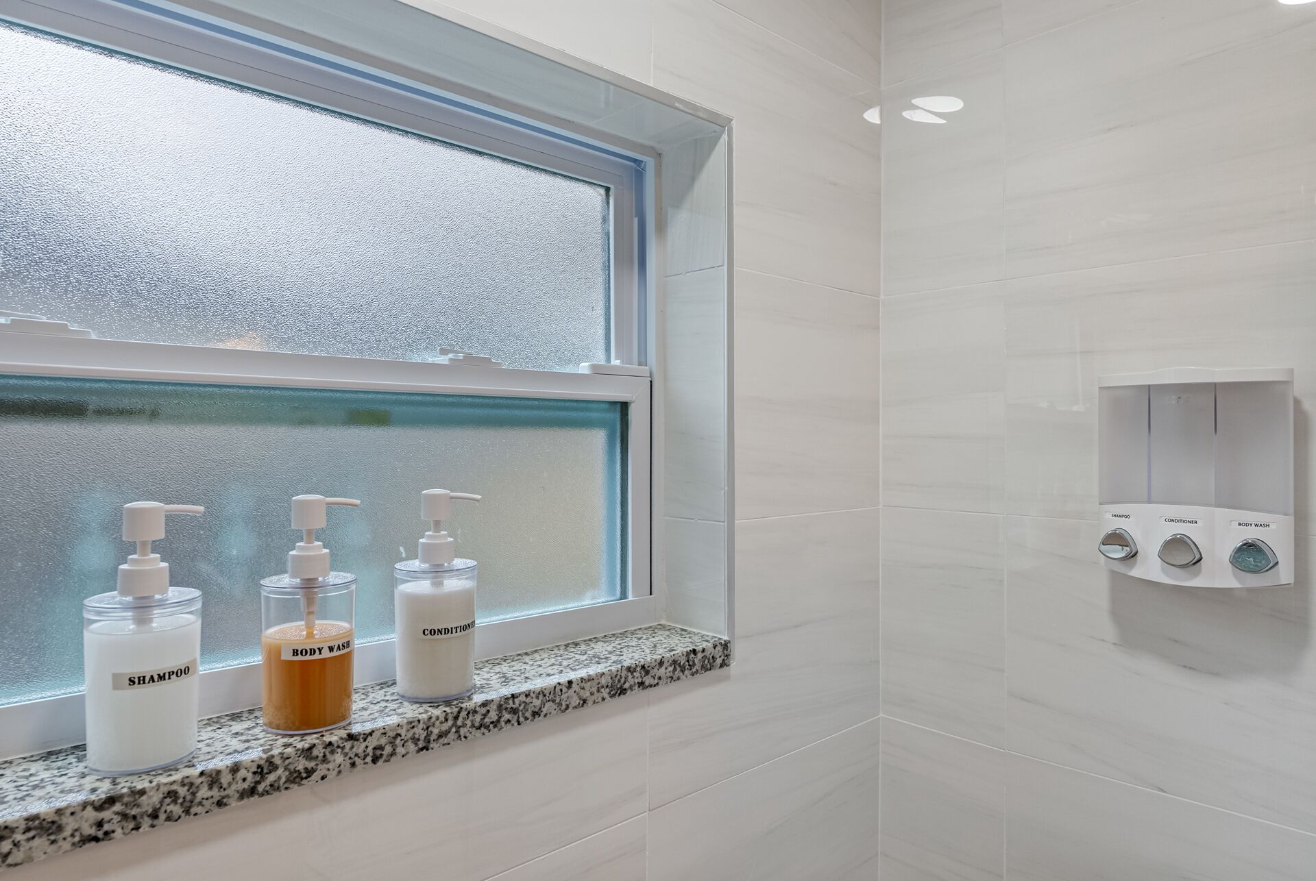 Une salle de bain avec une fenêtre, un lavabo équipé de distributeurs de savon et un espace douche avec un distributeur de savon.