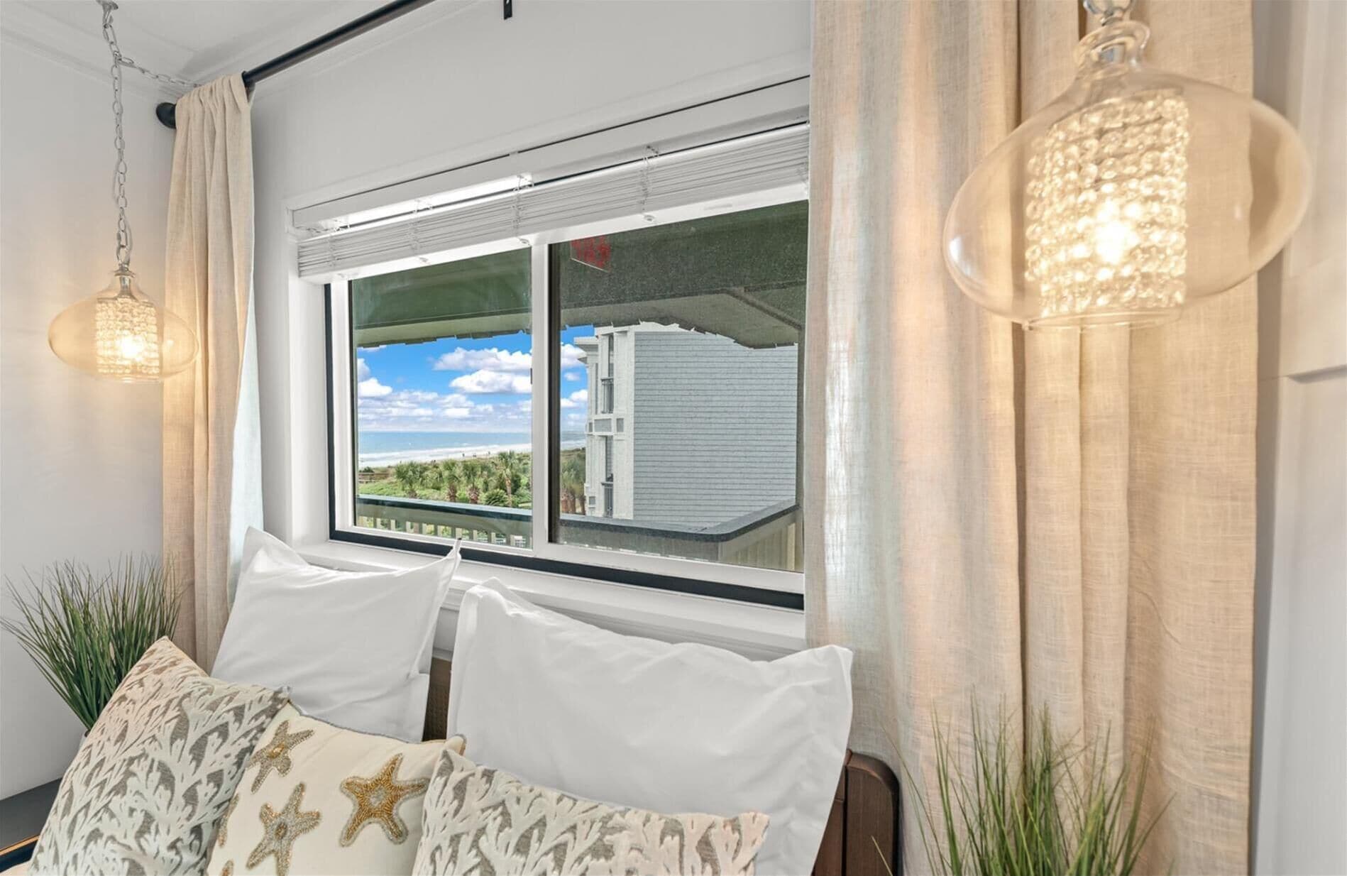 A room with a large window, a bed with white bedding, and two starfish-patterned pillows.