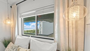 A room with a large window, a bed with white bedding, and two starfish-patterned pillows.