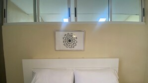A hotel room with a bed, white pillows, a nightstand, a remote control, and a decorative wall piece. - Dorado Vacation Home-Wi-Fi & AC (Dorado)
