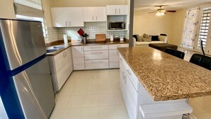 A modern kitchen with white cabinets, a granite countertop, a stainless steel refrigerator, and a microwave. - Dorado Vacation Home-Wi-Fi & AC (Dorado)