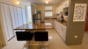 A modern kitchen with a central island, two bar stools, a refrigerator, and a microwave. - Dorado Vacation Home-Wi-Fi & AC (Dorado)