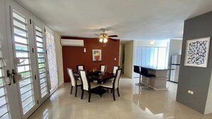 A spacious dining area with a dark wooden table and white chairs, a ceiling fan, and a window with blinds. - Dorado Vacation Home-Wi-Fi & AC (Dorado)