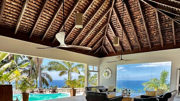 Amplia sala de estar con un gran ventanal que da a una piscina y al océano, con techo de paja y muebles modernos.