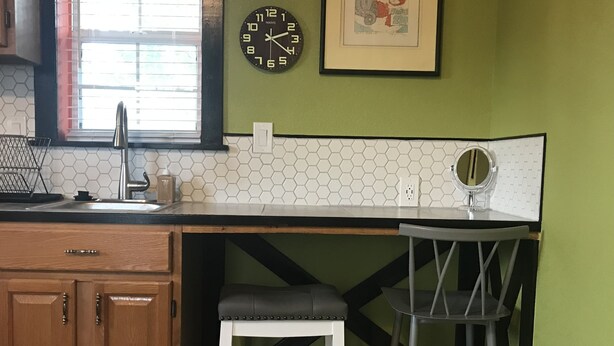 A kitchen with a wooden cabinet, a sink, a stool, a chair, a clock, and a framed picture on the wall. - Cozy Efficiency Studio/A near DownTown (San Antonio)