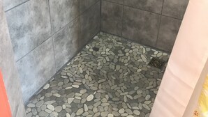 A shower area with grey tiled walls and a pebble-patterned floor. - Cozy Efficiency Studio/A near DownTown (San Antonio)